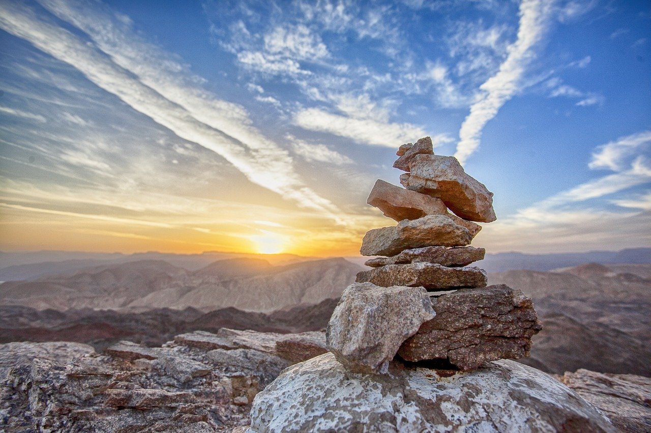 picture of inukshuk in a sunset overlooking a valley and mountains